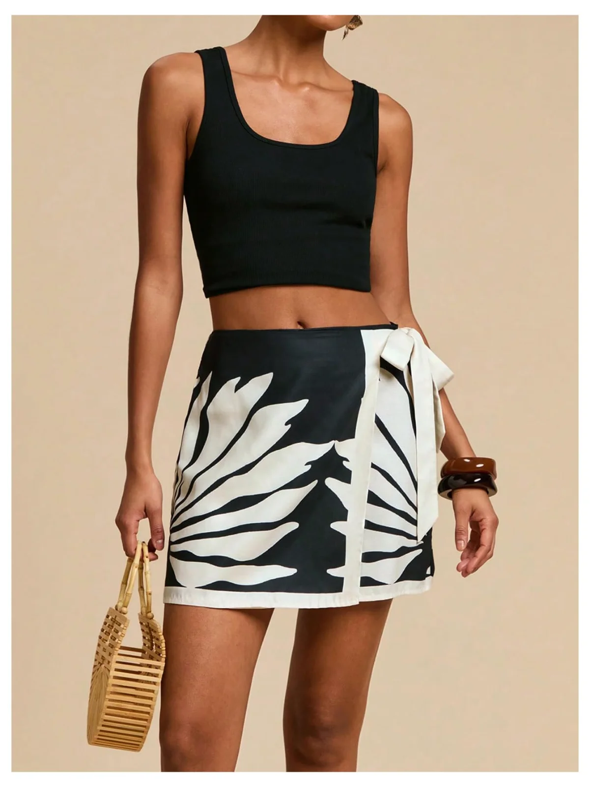 The wrap mini skirt in a black-and-cream leaf print, worn with a black tank and a raffia clutch