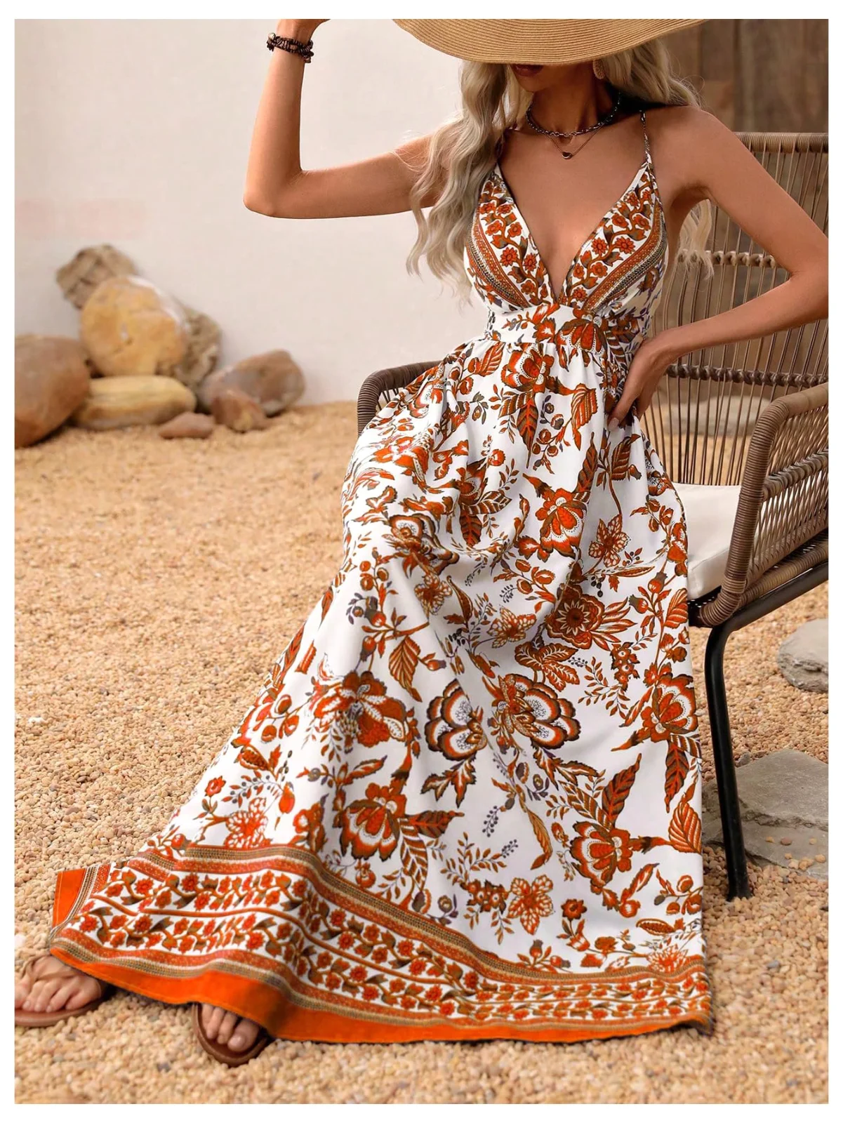 The backless flowy maxi dress in orange floral, under a straw hat, on a garden bench