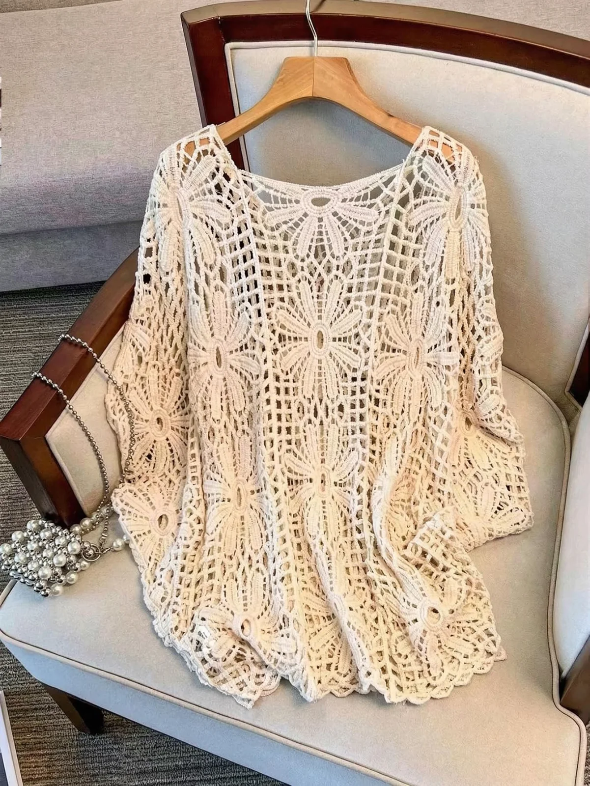 The crochet beach cover-up in beige, laid over the arm of a grey sofa
